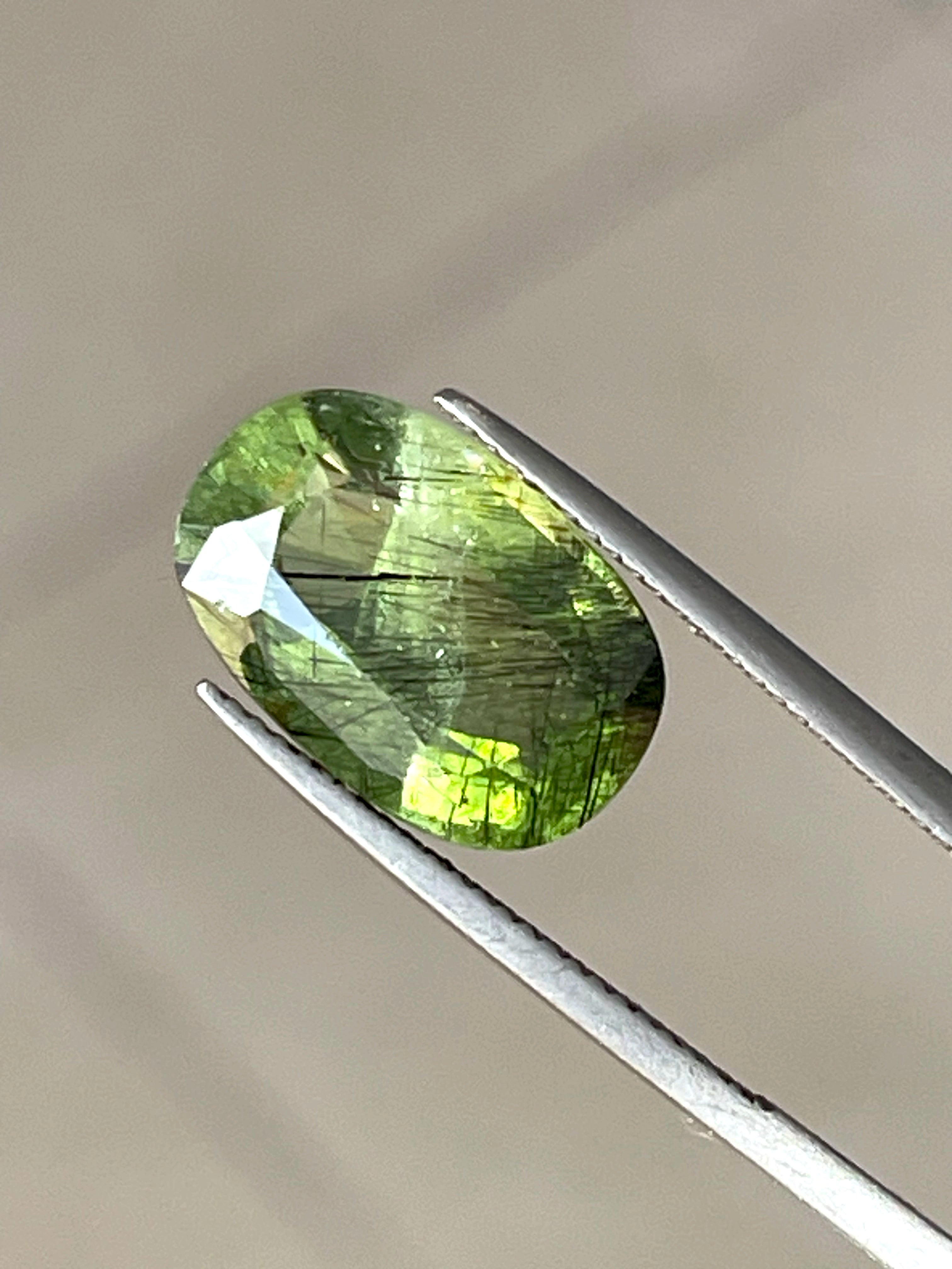 Oval-cut green Peridot with dark Ludwigite veins on white background