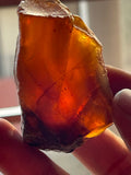 A rough amber stone specimen held between fingers, displaying a translucent orange color.