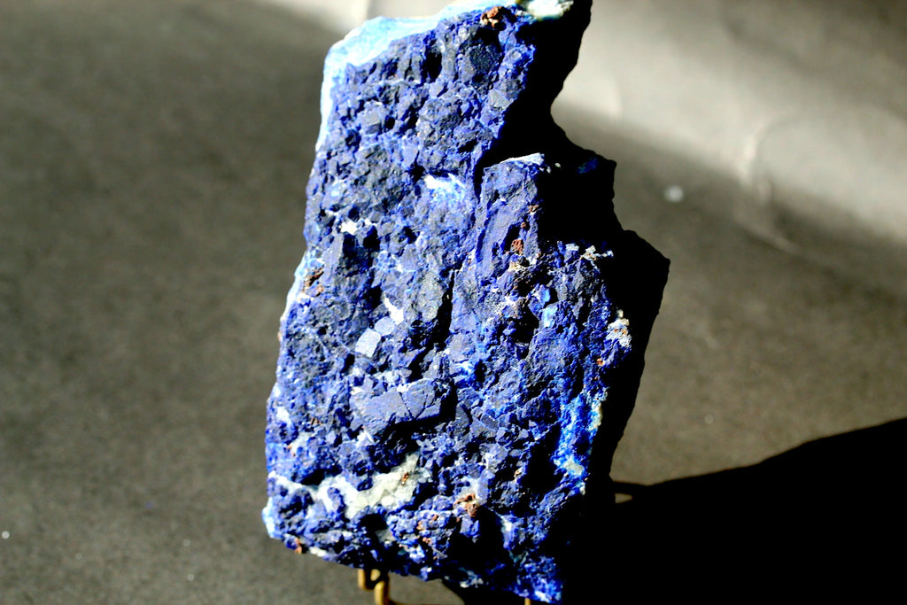 A rough,lazurite stone specimen standing upright on a small stand against a dark gray background.