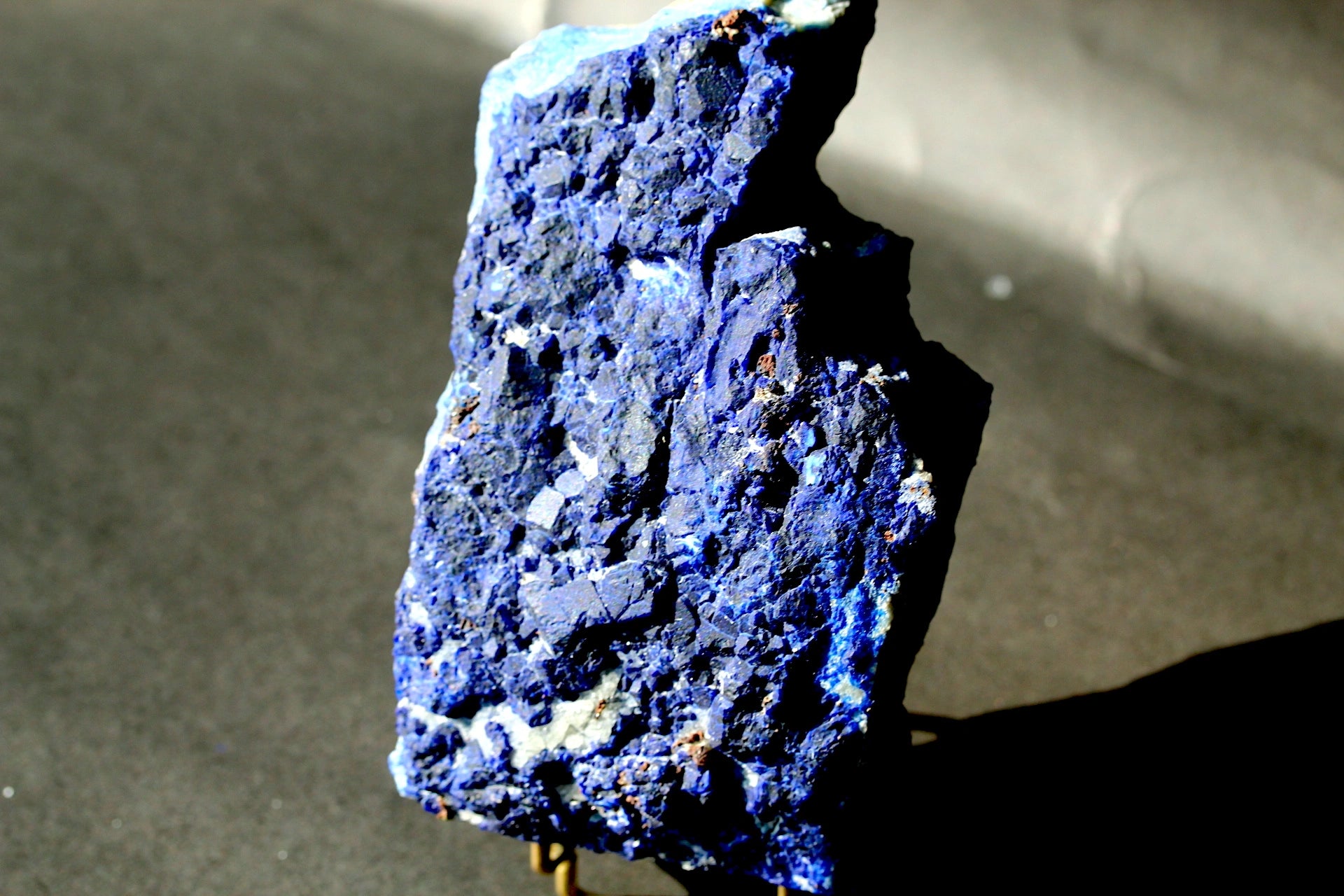A rough,lazurite stone specimen standing upright on a small stand against a dark gray background.