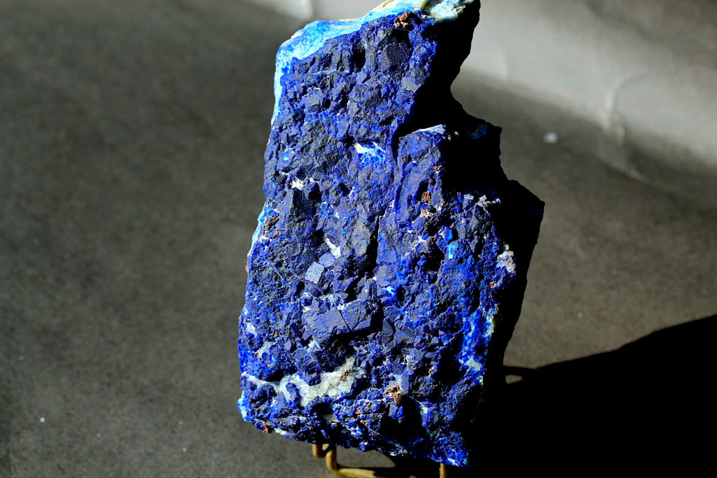 Natural Lazurite Specimen big size with deep blue and purple matrix, standing on a small display stand against a dark gray background.