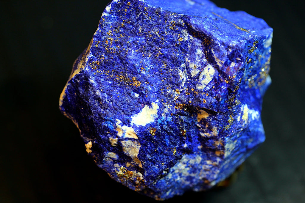 A close-up of a rough lapis lazuli crystal showing deep blue coloration with prominent golden pyrite inclusions 