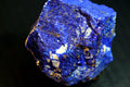 A close-up of a rough lapis lazuli crystal showing deep blue coloration with prominent golden pyrite inclusions 