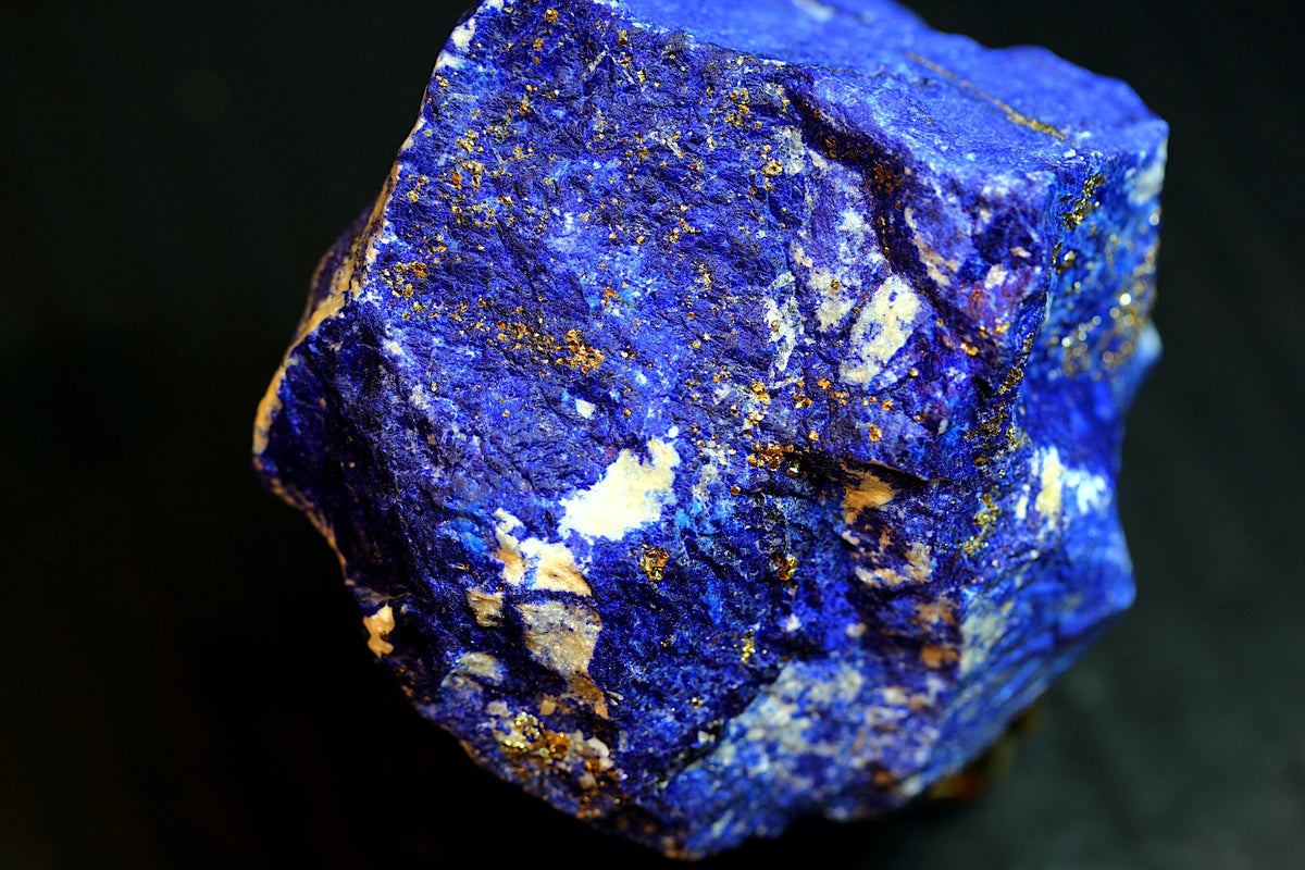 A close-up of a rough lapis lazuli crystal showing deep blue coloration with prominent golden pyrite inclusions 