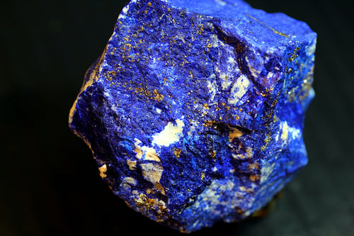 A close-up of a rough lapis lazuli crystal showing deep blue coloration with prominent golden pyrite inclusions 