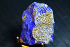 A raw blue lapis lazuli crystal specimen with prominent metallic gold pyrite inclusions, mounted on a small gold-colored 