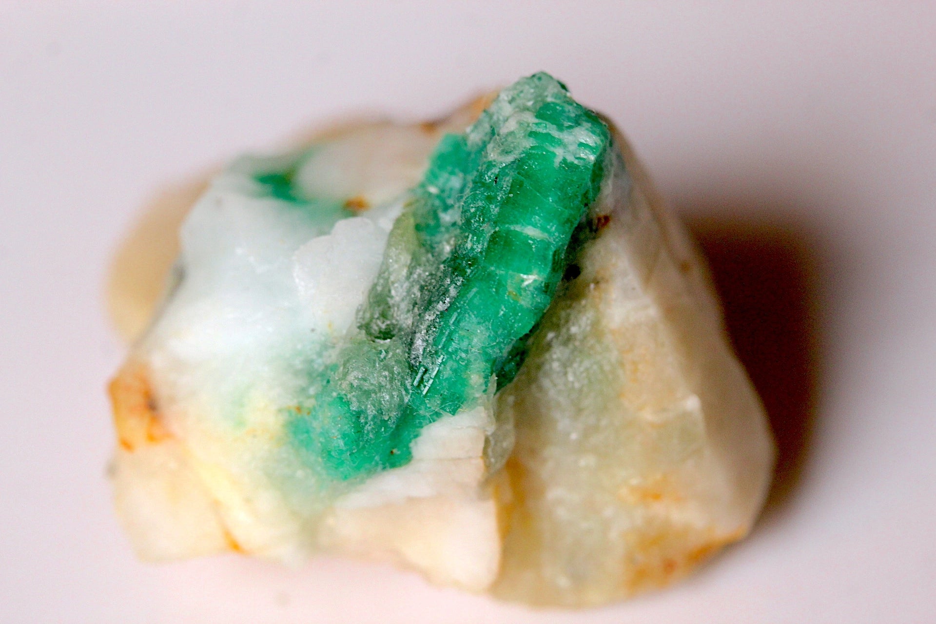 A raw green emerald stone or mineral specimen with a mix of vivid emerald green and milky white areas, resting on a plain light background.