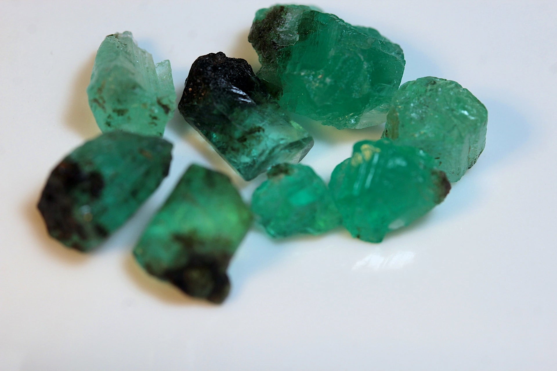 Several rough, raw emerald crystals with natural dark inclusions for lapidary
