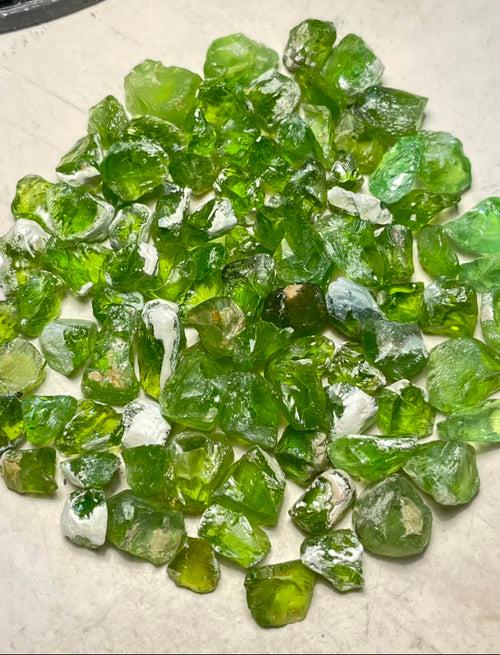A pile of rough, polished green PERIDOT gemstoen deal for lapidary 