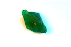 A raw, rough green emerald crystal with natural facets and tiny inclusions